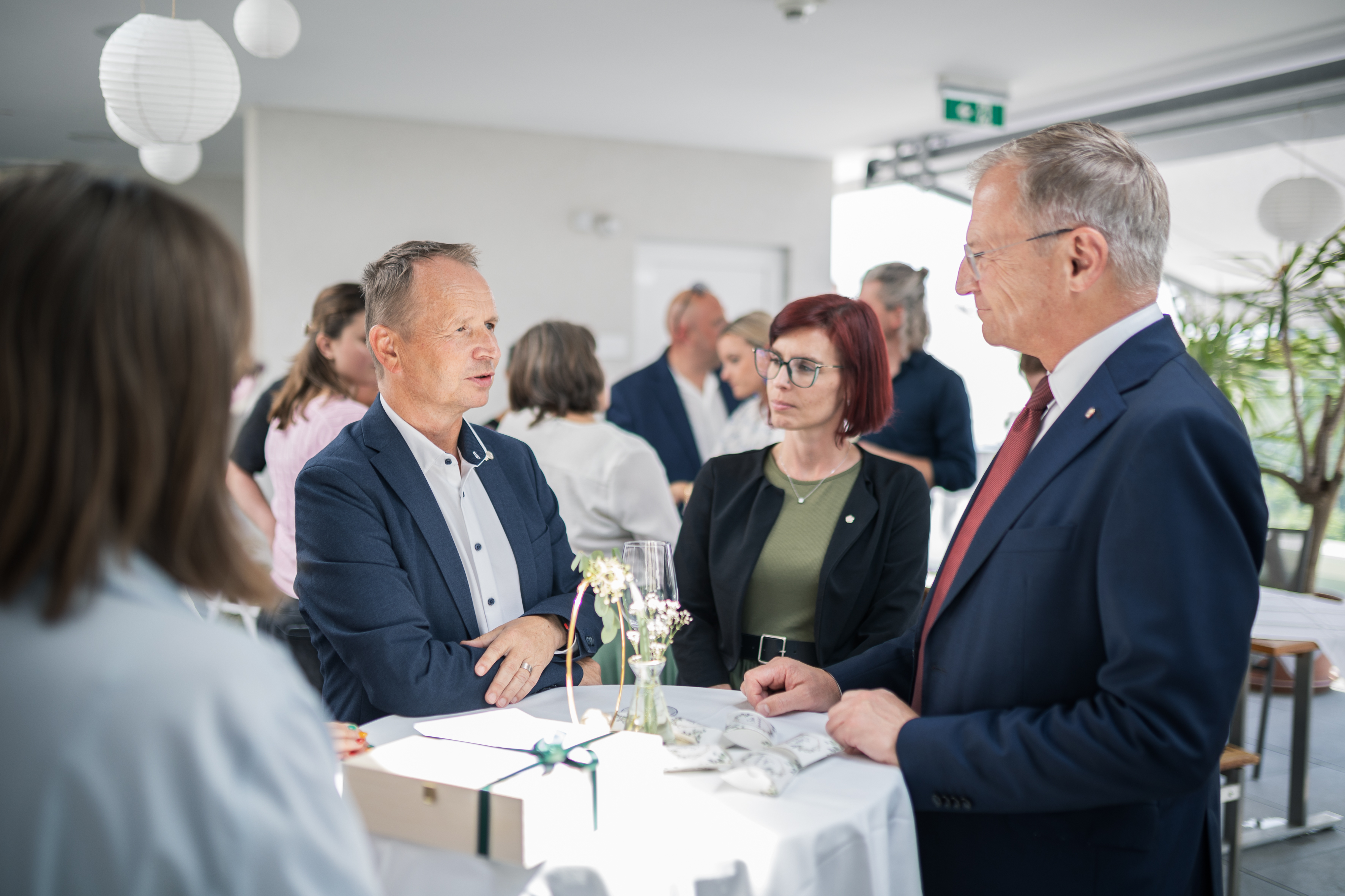 Landeshauptmann im Gespräch / Land OOE Der Landeshauptmann spricht an einem runden Stehtisch mit einem Mann und einer Frau.